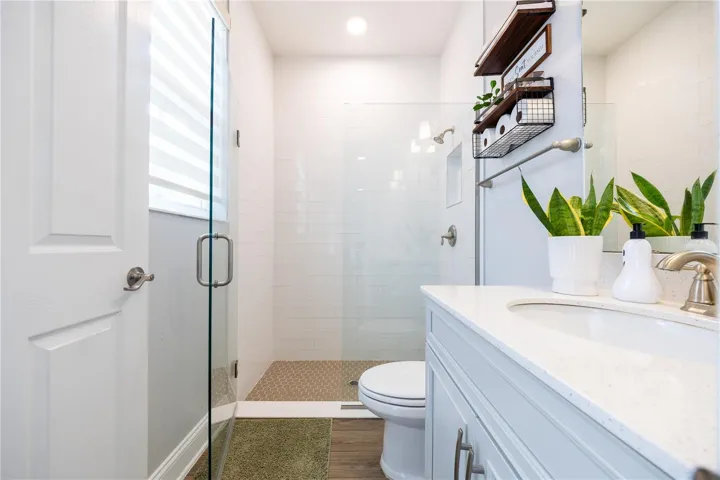 Bright bathroom featuring a frameless glass shower, white tile walls, mosaic shower floor, and a spacious vanity countertop.