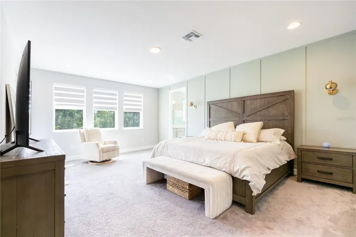 Spacious primary bedroom with an elegant accent wall, sitting area, and porch access with views of a conservation area.