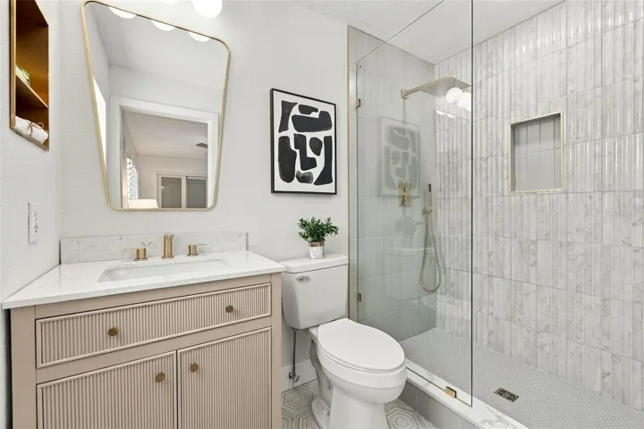 Primary bathroom with hexagon flooring, Quartz vanity, seamless glass shower with gleaming tile finish
