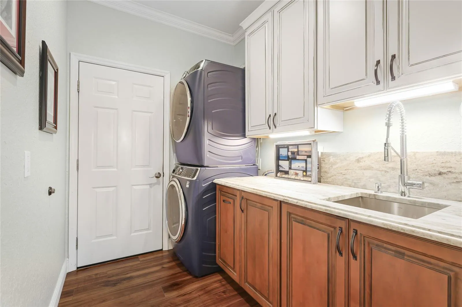 New laundry room featuring custom cabinetry, granite counter with backsplash, and stacked GE profile washer &amp; dryer.