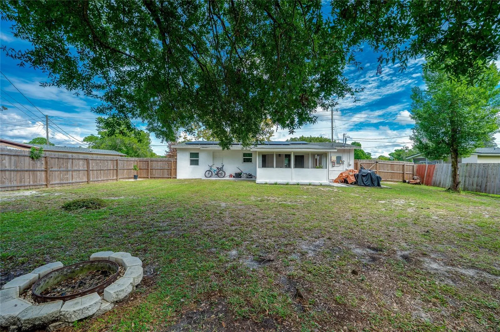 Generous rear lawn featuring a stone fire pit ring, full wood fencing, and direct views of the home's screened patio extension.