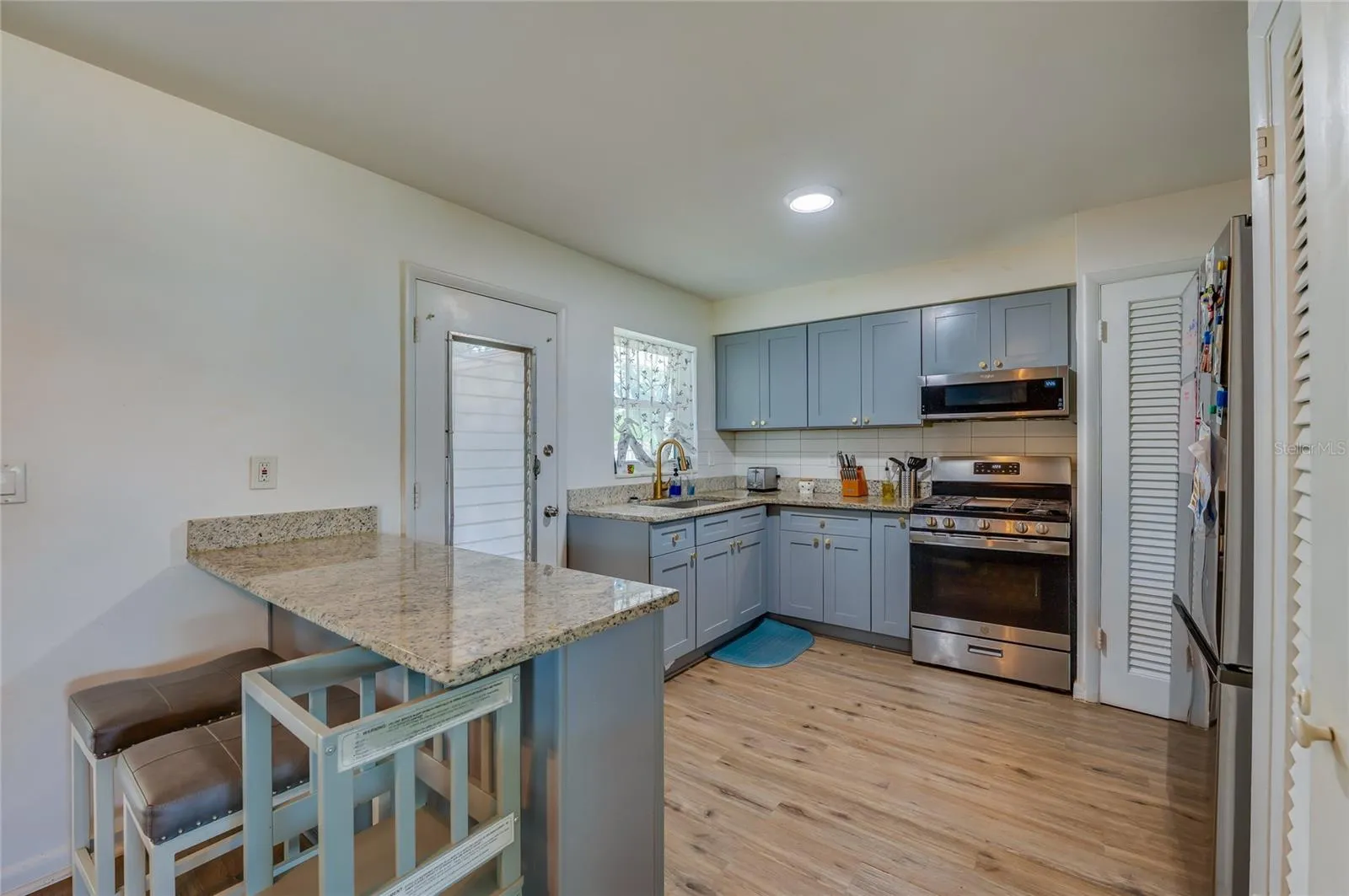 Functional kitchen layout displaying blue cabinetry, granite counter space, stainless steel appliances, and built-in breakfast bar overhangs.