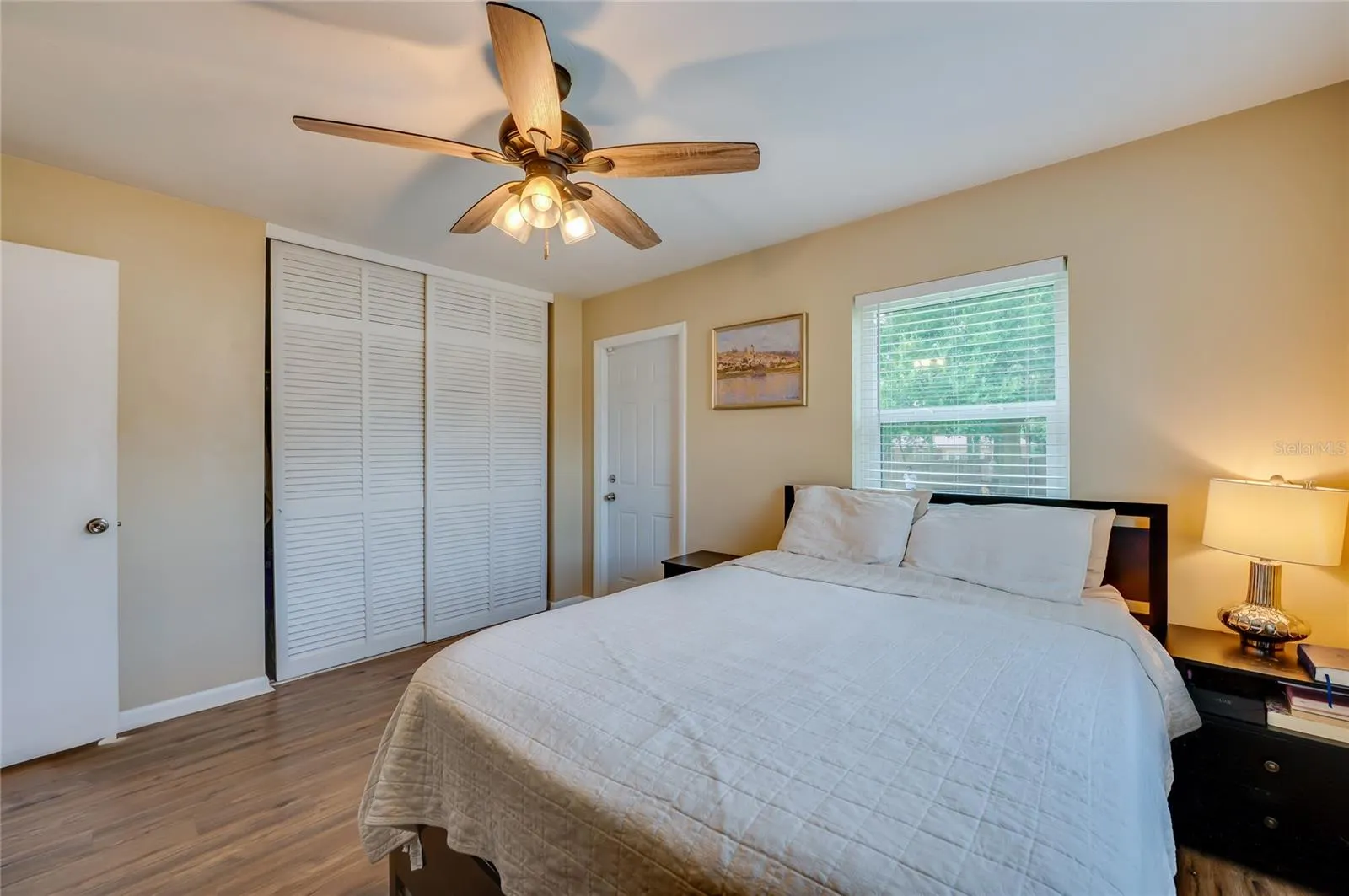 Spacious bedroom featuring warm LVP flooring, white louvered sliding closet doors, and multiple windows allowing plenty of natural light.