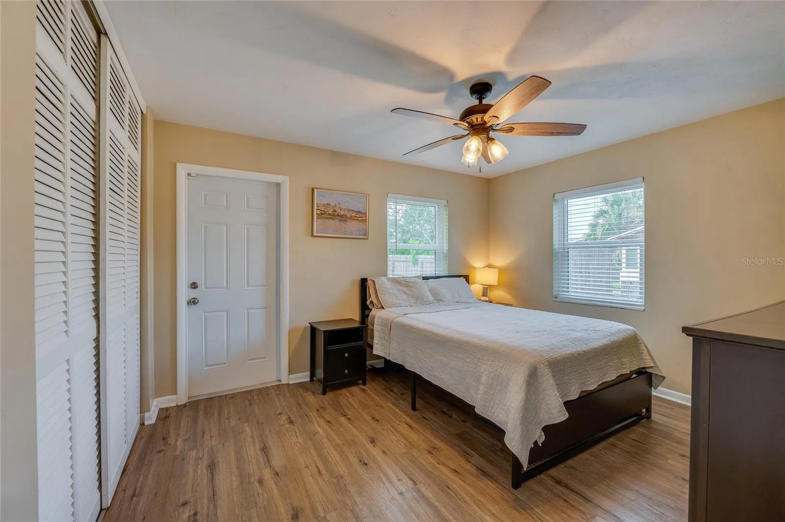 Cozy bedroom offering LVP flooring, louvered closet doors, neutral walls, and a ceiling fan with integrated lighting.