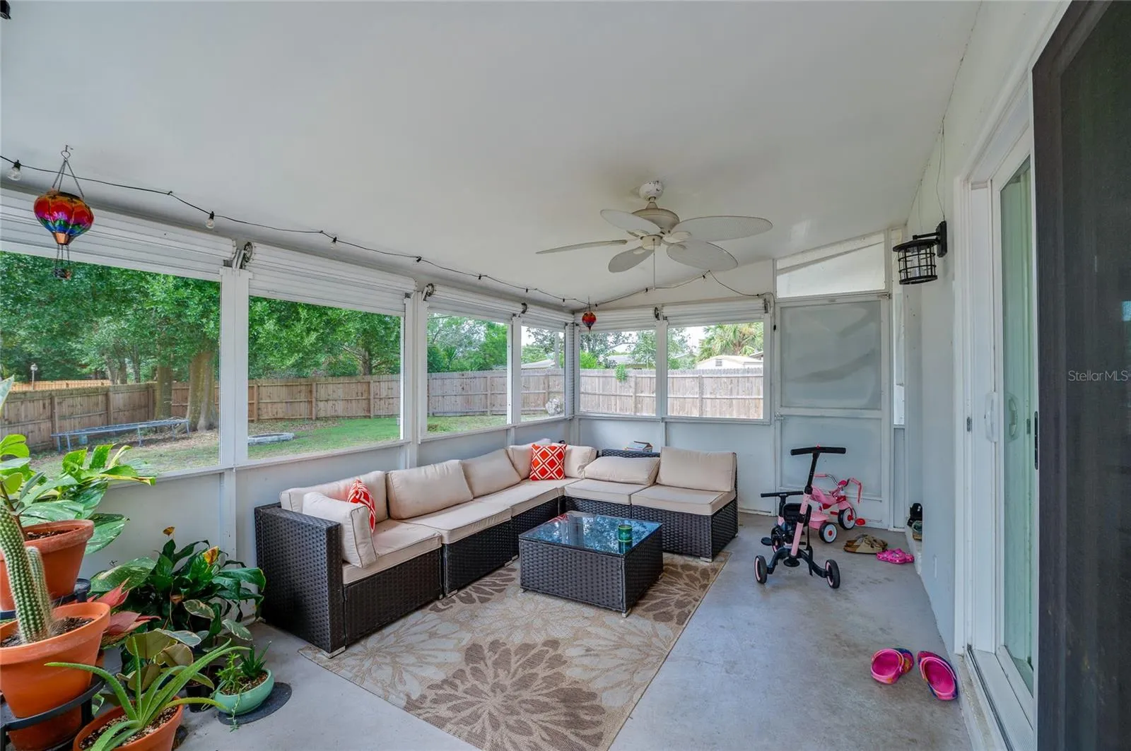 Enclosed, screened-in porch with ceiling fans and surrounding mesh screens overlooking the fenced backyard area.