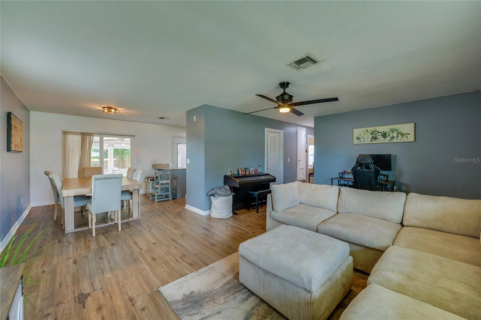 Broad view of an open layout emphasizing natural LVP floors, a ceiling fan, and clear sightlines between living and dining spaces.