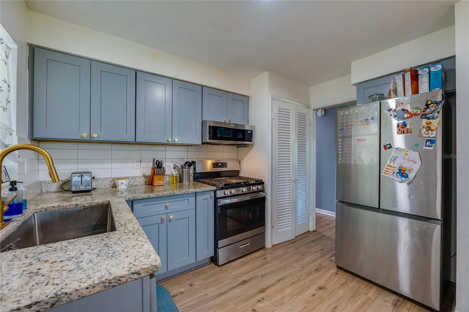 Modernized kitchen with stylish gray-blue cabinets, granite countertops, tile backsplash, and a large stainless steel refrigerator.