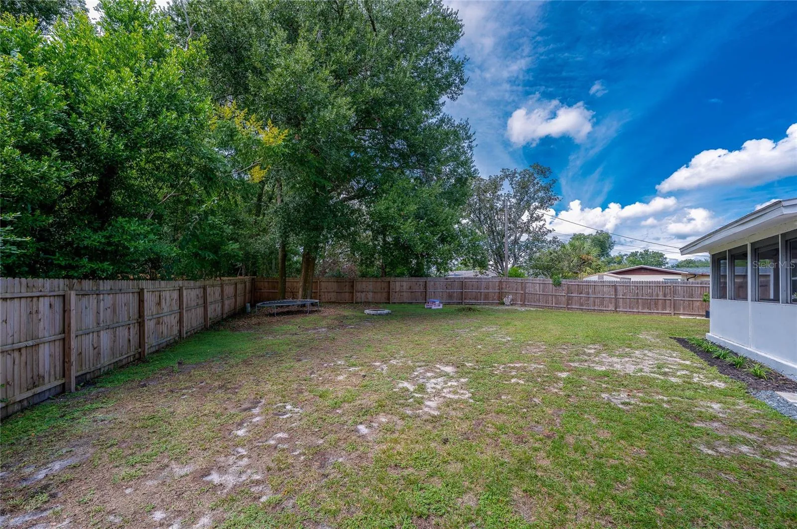Spacious backyard enclosed by a full wooden privacy fence and lined with mature trees along the perimeter.