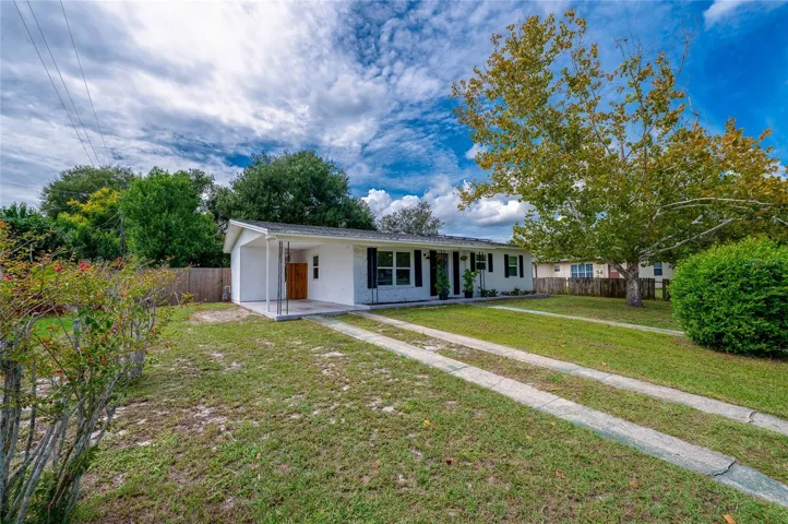 Exterior view highlighting the long concrete ribbon driveway, expansive front lawn, mature shade trees, and low-maintenance single-story design.