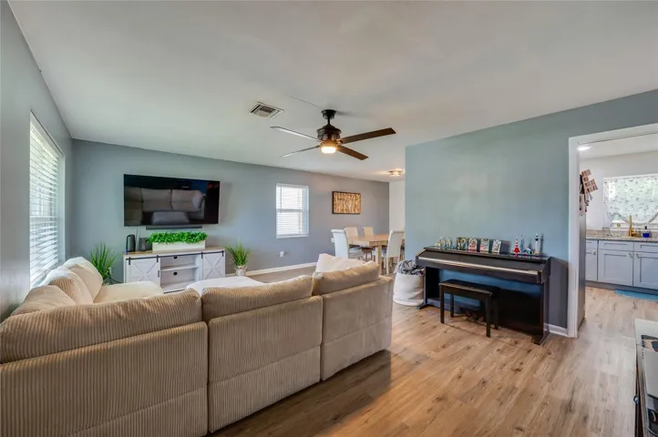 Expansive open-concept living space with LVP flooring, ceiling fans, and seamless flow into adjoining dining and kitchen areas.
