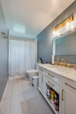 Bathroom displaying a single vanity with gold hardware, modern lighting fixtures, neutral tile flooring, and clean wall finishes.