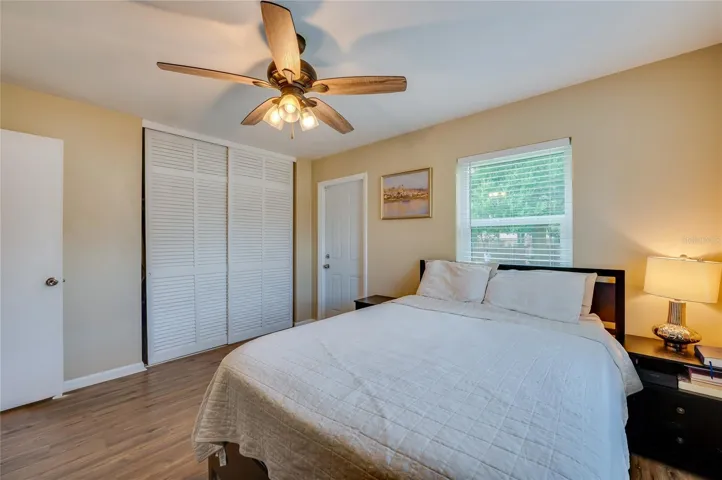 Spacious bedroom featuring warm LVP flooring, white louvered sliding closet doors, and multiple windows allowing plenty of natural light.