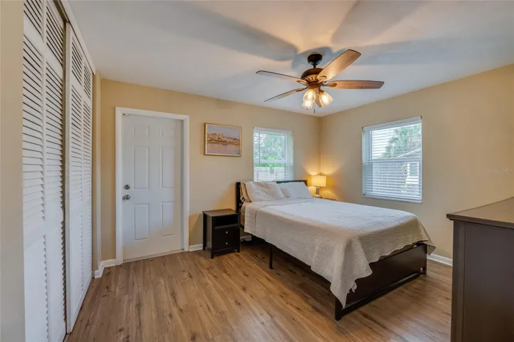 Cozy bedroom offering LVP flooring, louvered closet doors, neutral walls, and a ceiling fan with integrated lighting.