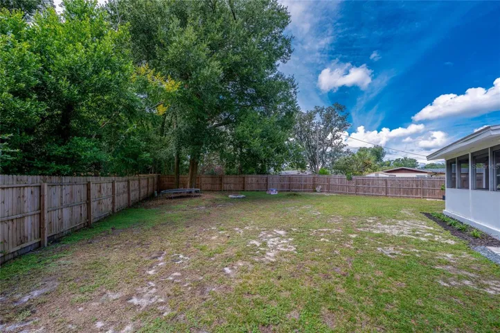 Spacious backyard enclosed by a full wooden privacy fence and lined with mature trees along the perimeter.