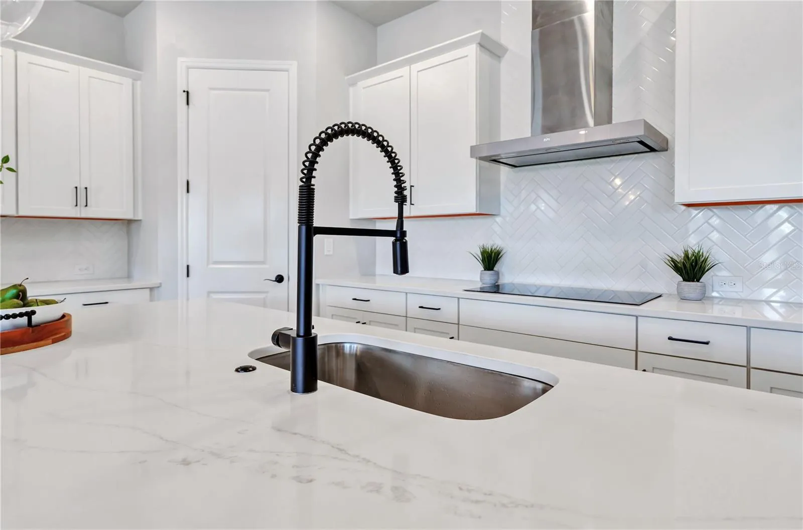 Quartz counters, undermount sink, matte black faucet, and herringbone tile backsplash with a view into the home.