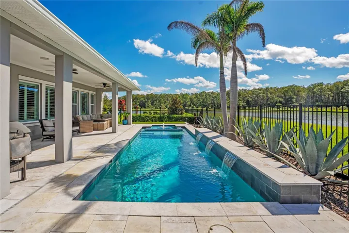 Heated salt water pool viewed from the covered lanai with palms and a water view.