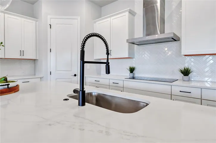 Quartz counters, undermount sink, matte black faucet, and herringbone tile backsplash with a view into the home.