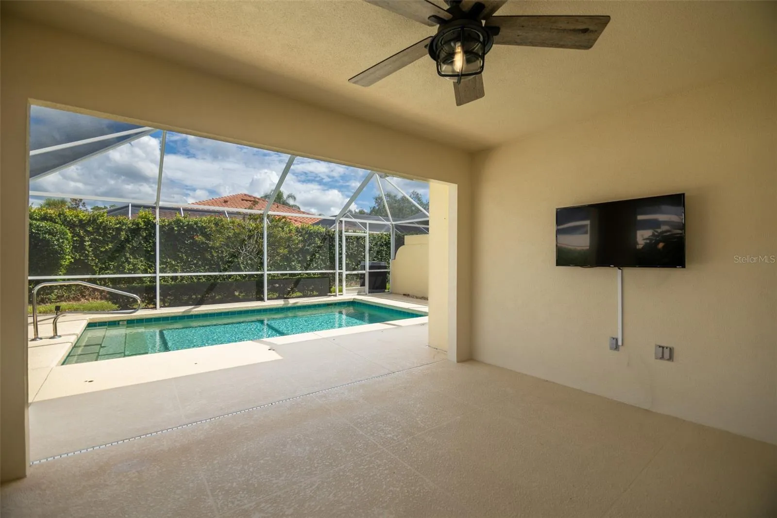 Back patio view of the pool in the center and wall mounted tv on the right.