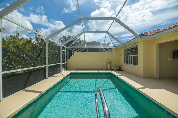 View of pool and pool equipment as well as another screen door at the back of the screen cage.