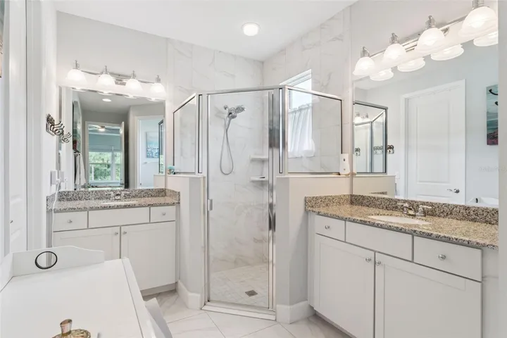 8' x 15' Primary Bathroom w/ separate granite countertop vanities, glass enclosed walk-in shower &amp; bench seat