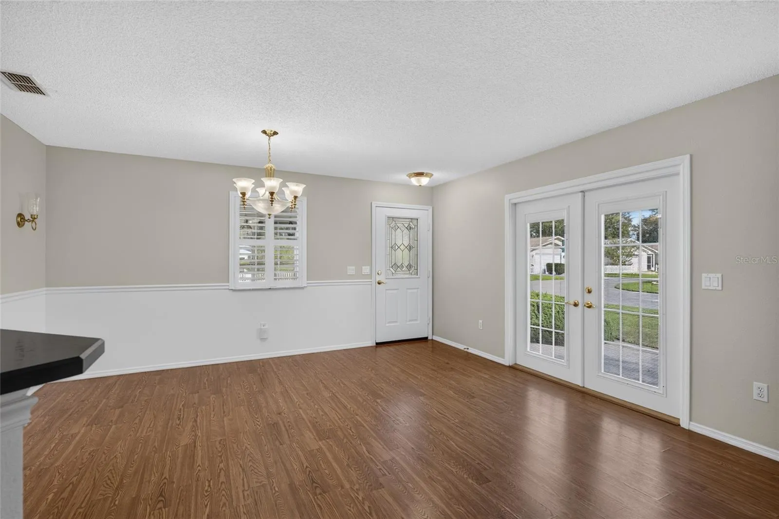 Close up view of DINING ROOM - Chair rail woodwork, decorative wall sconces (back L), and matching chandelier & pendant lighting add distinctive detail. Note the French doors which access the side patio on eastern side of home.