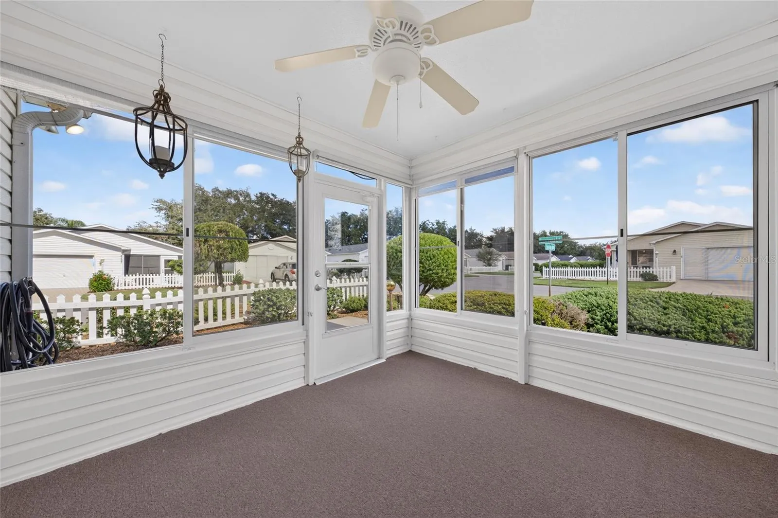 ENCLOSED LANAI - Plexiglass windows surround a bright sitting area with a ceiling fan and offers views of the landscaping and the corner of Escobar Ave & Elana Place.