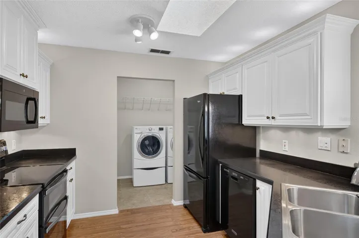 KITCHEN View - Showcases raised-panel white cabinetry with crown molding and over & under cab lights. A SKYLIGHT illuminates the kitchen w/ NATURAL LIGHT. Note that black appliances provide a dramatic contrast of color.