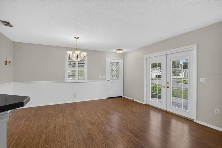 Close up view of DINING ROOM - Chair rail woodwork, decorative wall sconces (back L), and matching chandelier & pendant lighting add distinctive detail. Note the French doors which access the side patio on eastern side of home.