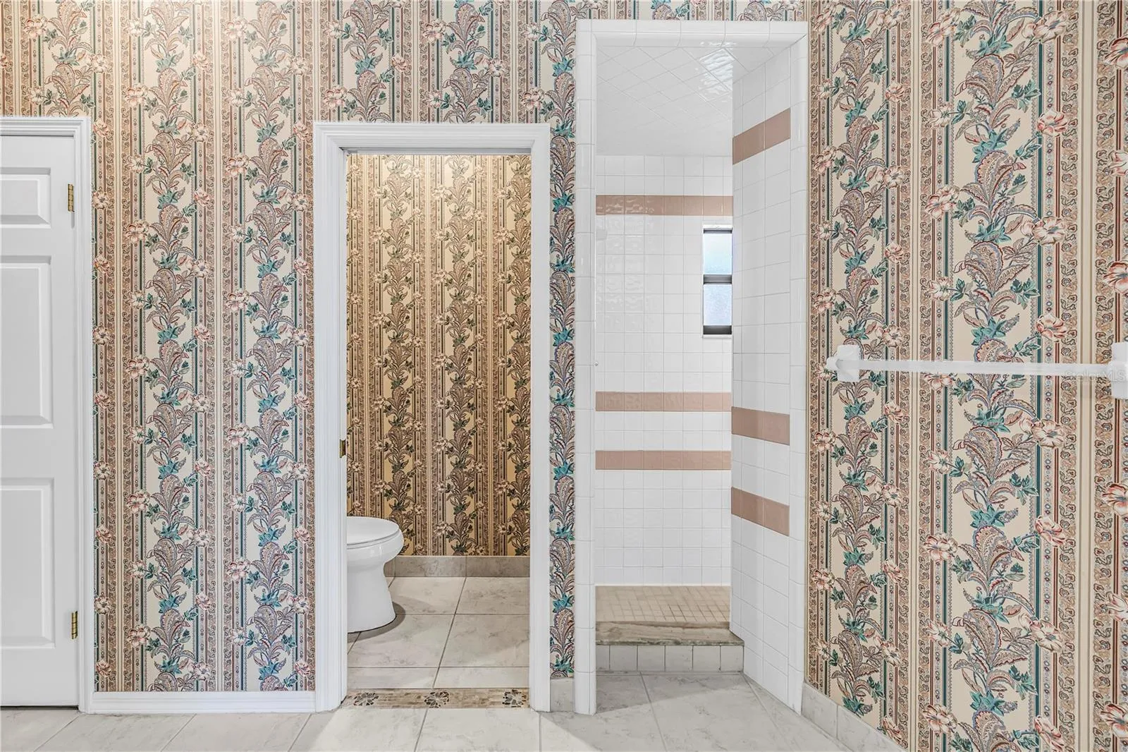 Current Photo of primary bathroom with toilet room and entry to shower.  Again reference wall with towel bar for shower enclosure