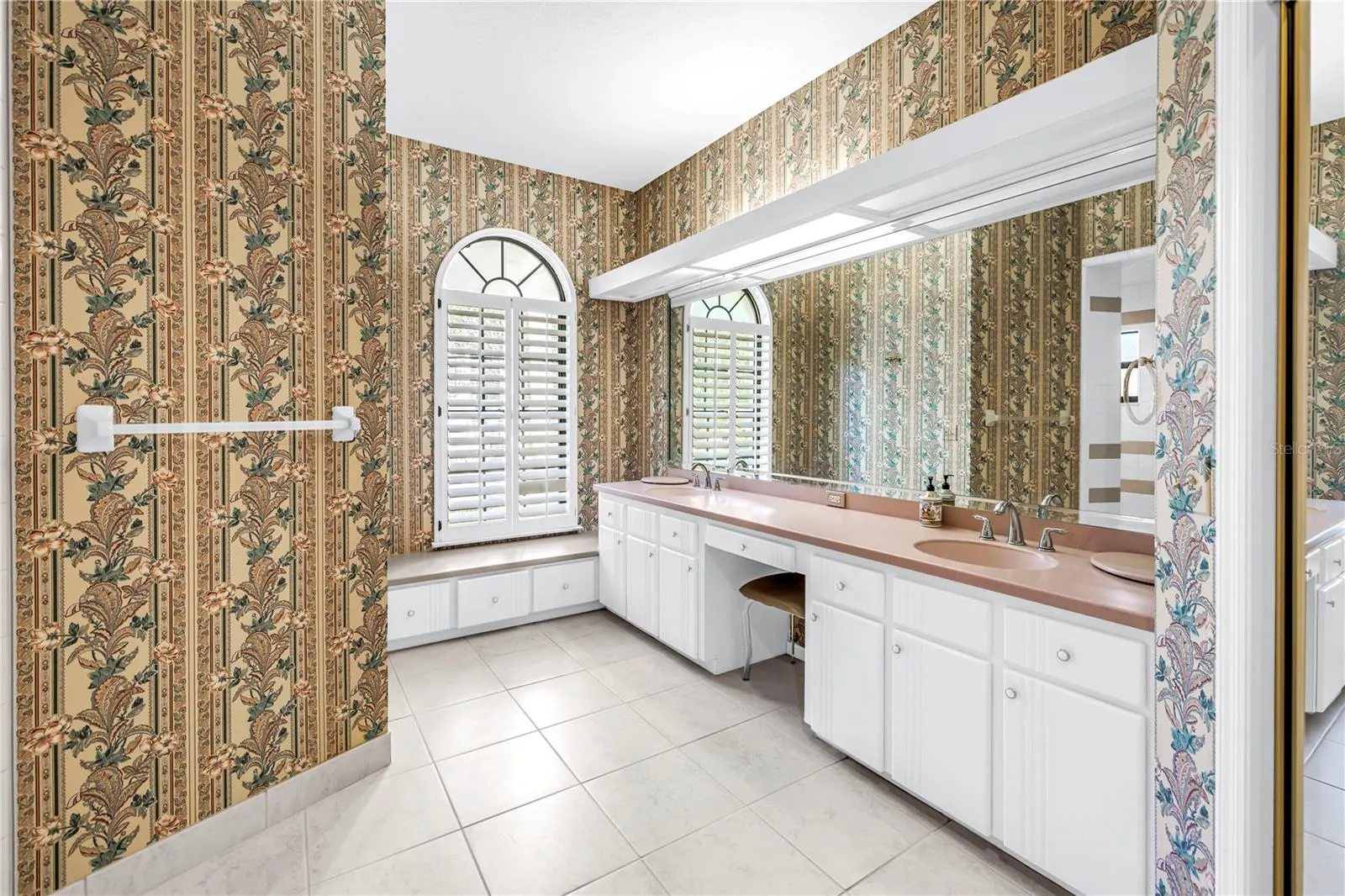 Current Photo of Primary Bath with long dual Vanity and dressing table.  Shower is behind wall with towel bar.