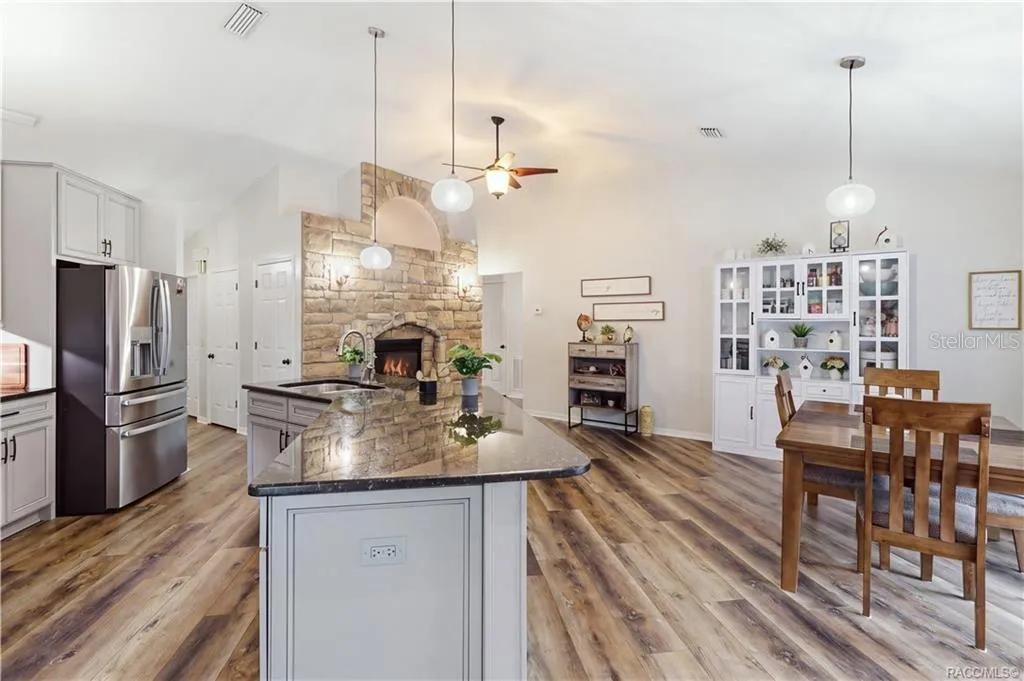 KITCHEN & DINING VIEW- Spacious kitchen & dining layout featuring a large granite island, vaulted ceilings & striking stone-accented fireplace.