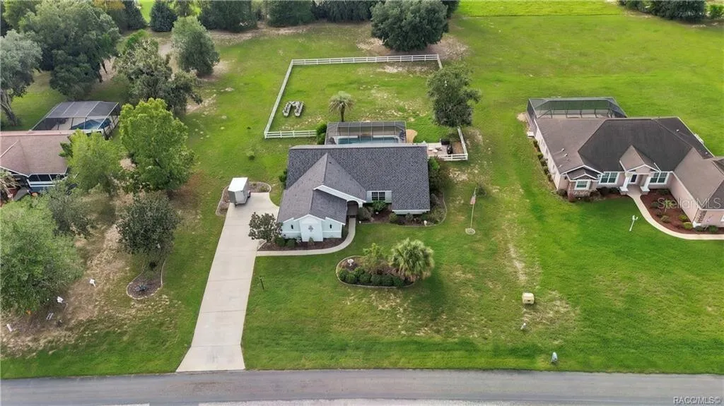 Aerial Property View – Beautiful overhead perspective showcasing the home, screened pool, white rail-fenced backyard & surrounding green space.