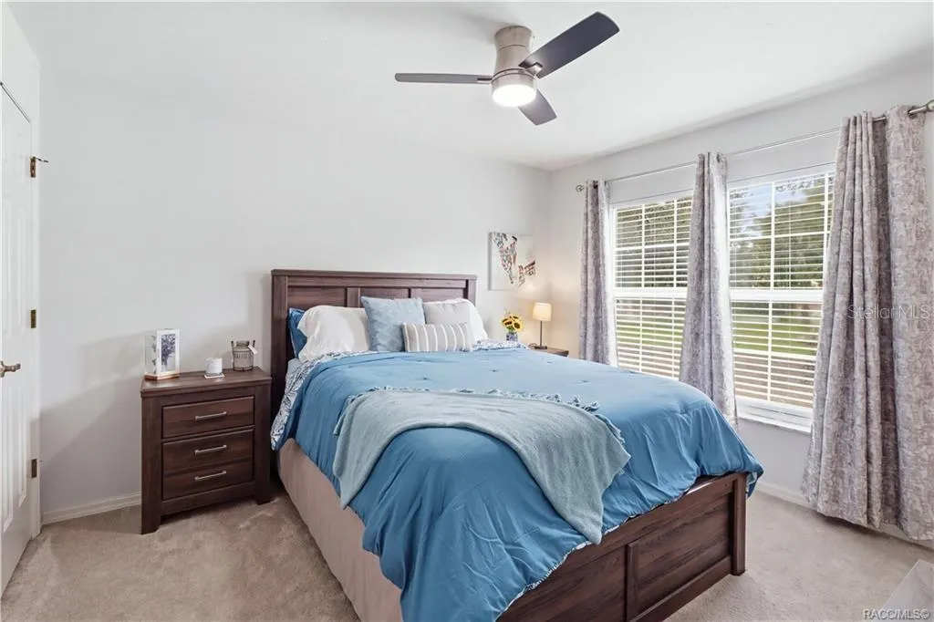 BEDROOMComfortable bedroom featuring neutral carpeting, ceiling fan & a large window overlooking the landscaped yard
