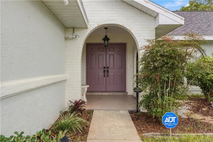 COVERED FRONT ENTRANCE- Inviting covered entrance featuring an attractive brick archway, double entry doors & decorative landscaping.