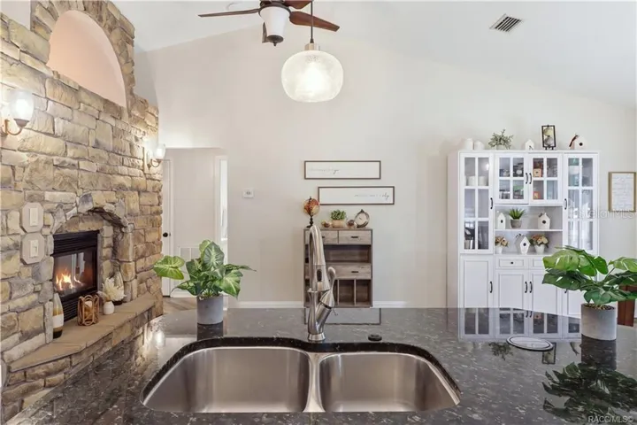 KITCHEN & FIREPLACE VIEWOpen kitchen showcasing the granite island, vaulted ceilings, stone-accented fireplace & adjoining dining area.