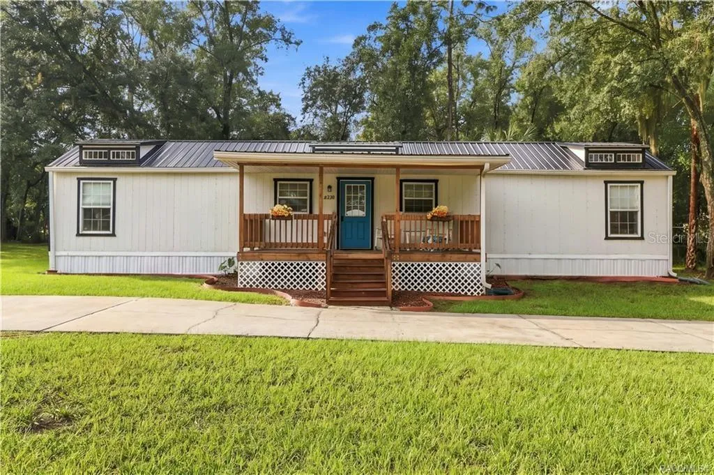 Front Elevation – Enjoy the home's charming curb appeal, featuring a welcoming covered porch, wooden railings, decorative roof details &amp; circular concrete driveway.