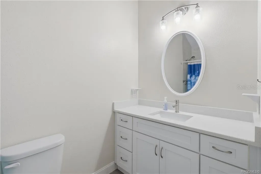 Primary Bathroom – Bright bathroom featuring a white vanity w/solid-surface countertop, undermount sink, oval mirror, attractive lighting &amp; convenient storage cabinetry.