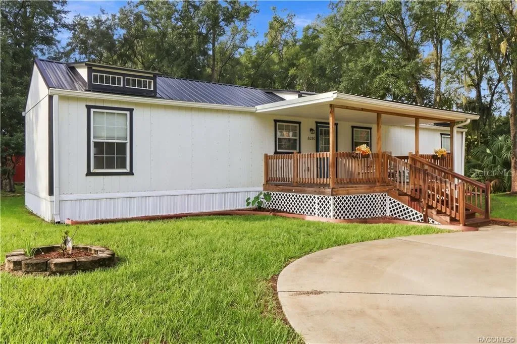 Front Exterior – Attractive white exterior w/contrasting dark trim, METAL ROOF &amp; spacious covered wooden porch, surrounded by a lush green lawn.