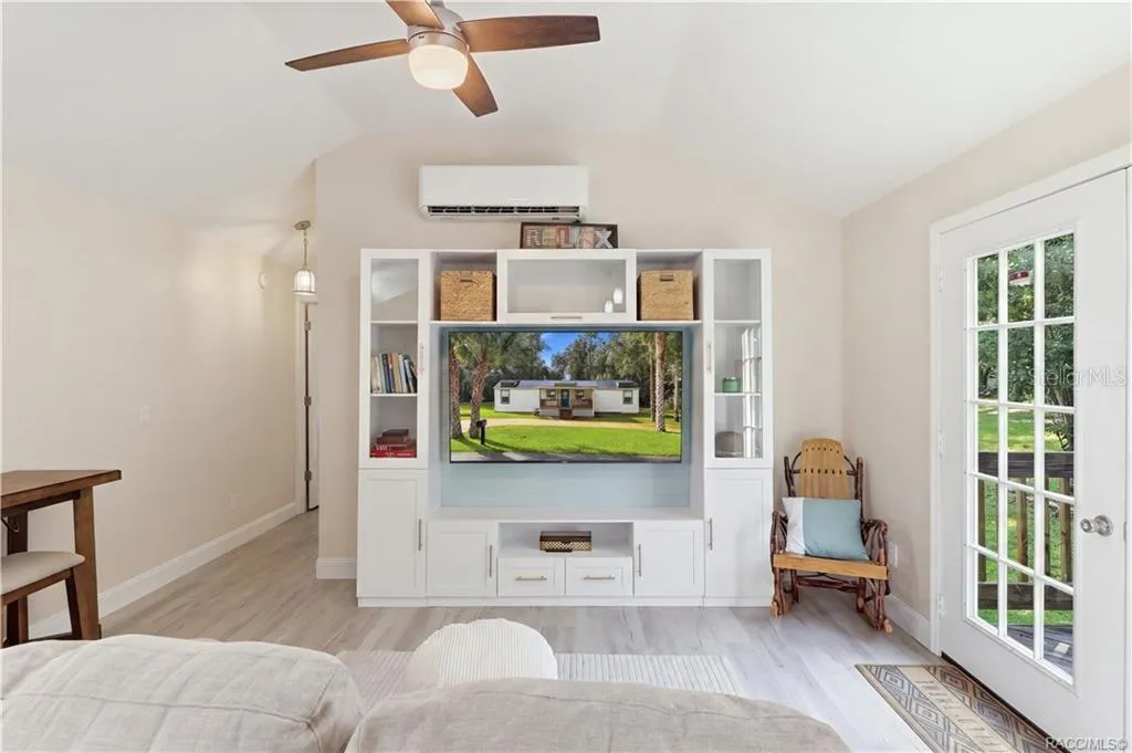 Living Room – Bright &amp; inviting living room featuring VAULTED CEILINGS, luxury vinyl plank flooring, ceiling fan, w/entertainment cabinetry &amp; a MINI-SPLIT HEATING &amp; COOLING SYSTEM. French doors provide views of the backyard &amp; access to the rear deck.