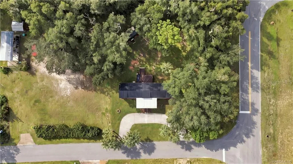 Aerial Property View – Beautiful overhead perspective showcasing the .29-ACRE CORNER HOMESITE, METAL ROOF, circular concrete driveway, mature shade trees &amp; spacious lawn.