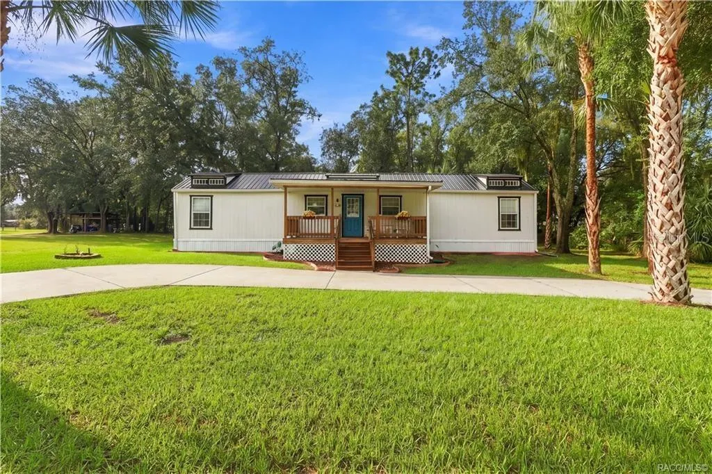 Charming Front Exterior – Beautifully presented home featuring a METAL ROOF, inviting COVERED FRONT PORCH, attractive landscaping &amp; a welcoming blue front door.