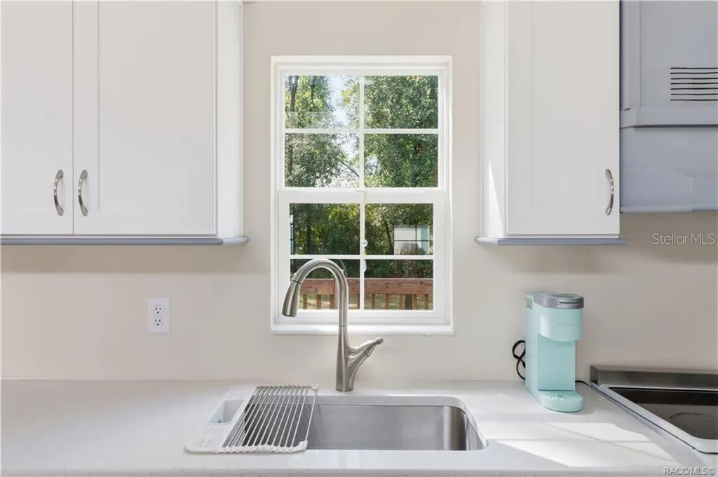 Kitchen Sink &amp; Window – Stainless-steel sink w/pull-down faucet, solid surface countertop &amp; window overlooking the greenery outside.