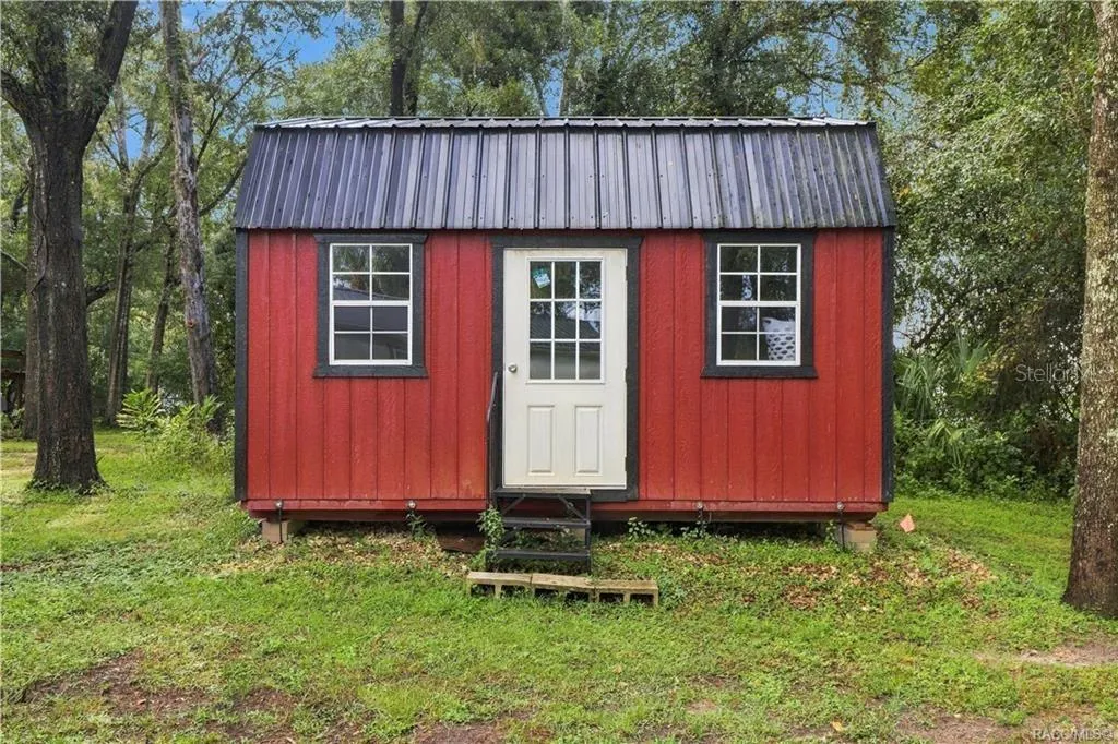 Detached Storage Building – Charming RED DETACHED STORAGE BUILDING featuring a METAL ROOF, double windows &amp; convenient entry door. A wonderful addition for storing lawn equipment, tools or outdoor essentials!