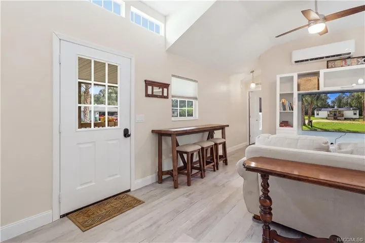 Living Area &amp; Front Entry – Welcoming living space featuring VAULTED CEILINGS, high transom windows, ceiling fan, attractive flooring &amp; a convenient seating area near the front entrance.