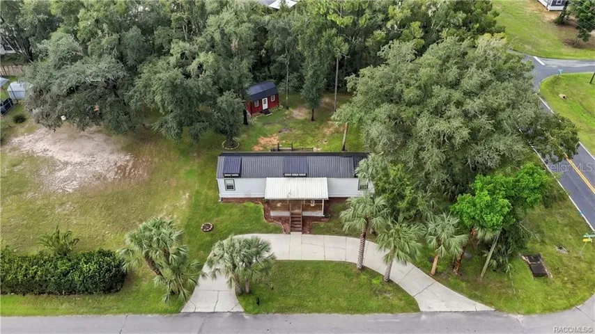 Aerial Property View – A beautiful overhead perspective of the .29-ACRE CORNER HOMESITE, showcasing the METAL ROOF, COVERED FRONT PORCH, circular concrete driveway, mature trees &amp; detached storage building.