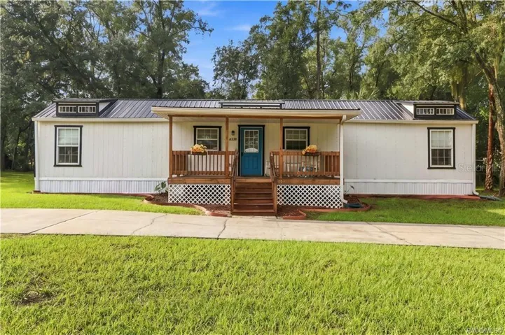Front Elevation – Enjoy the home's charming curb appeal, featuring a welcoming covered porch, wooden railings, decorative roof details &amp; circular concrete driveway.