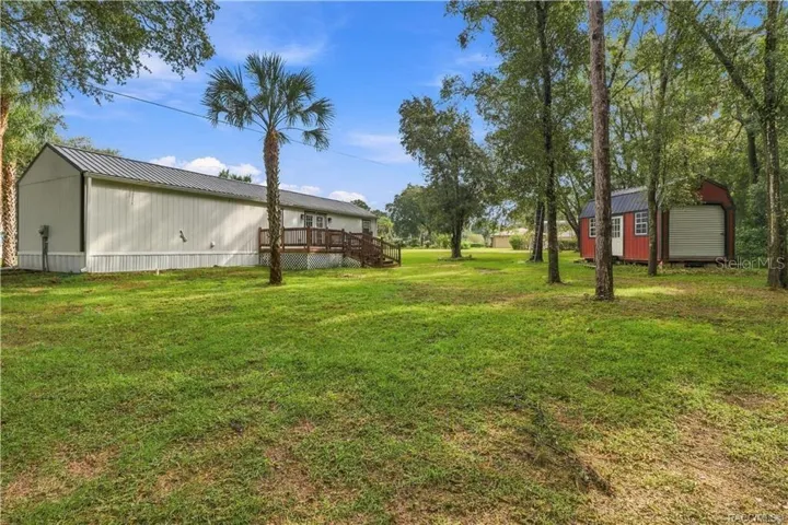 Backyard &amp; Storage Building – Spacious backyard featuring mature trees, open lawn, wooden deck &amp; a distinctive RED DETACHED STORAGE BUILDING w/metal roof &amp; roll-up door.