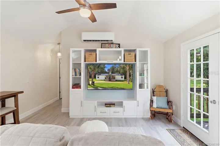 Living Room – Bright &amp; inviting living room featuring VAULTED CEILINGS, luxury vinyl plank flooring, ceiling fan, w/entertainment cabinetry &amp; a MINI-SPLIT HEATING &amp; COOLING SYSTEM. French doors provide views of the backyard &amp; access to the rear deck.