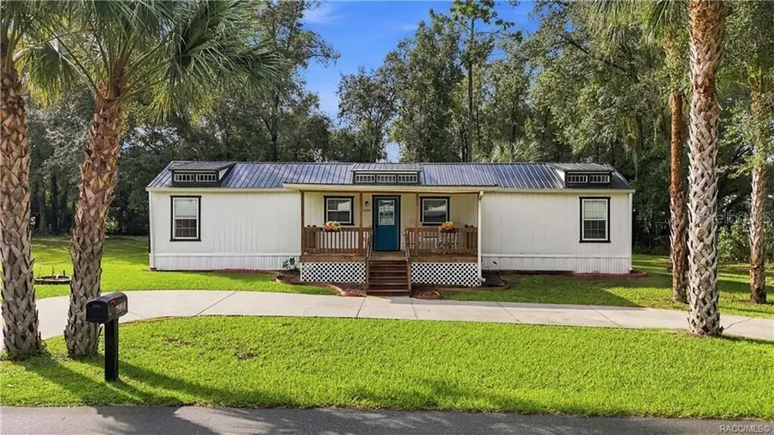 Welcome Home- Front Exterior – Attractive home featuring a METAL ROOF, COVERED FRONT PORCH, welcoming blue front door, wooden railings &amp; palm trees framing the property.