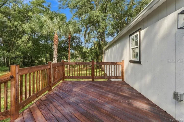 Rear Deck – Spacious wooden deck featuring sturdy railings &amp; room for outdoor seating, surrounded by Florida greenery &amp; mature palms.